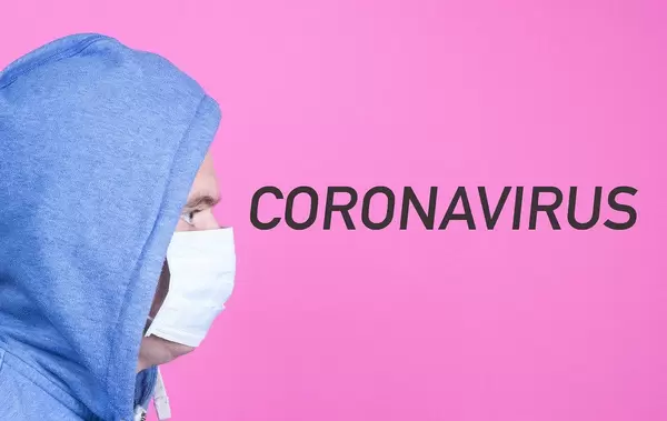 Man mit Pullover trägt eine Gesichtsmaske und schaut auf das Wort Coronavirus auf pinkem Hintergrund