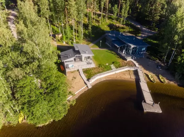 Man on a wooden jetty takes Ariel shot  of the guest house Villa Jolla at Finland's longest lake Päijänne, with canoes and nordic forest in the background