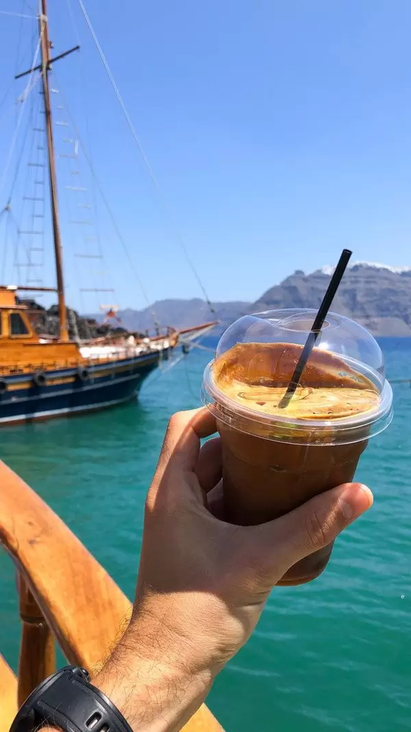 Man on vacation holds a coffee to go in his hand, in front of the Aegean Sea near Santorini, Greece