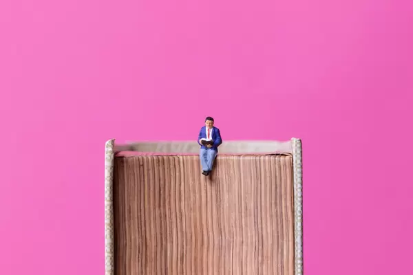 Man sitting on book with pink background