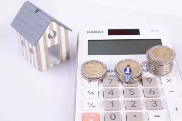 Man sitting on coin stack with calculator and small house