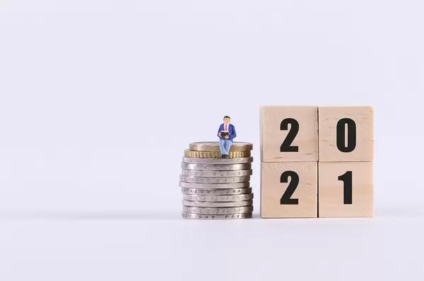 Man sitting on stack of coins and wooden cubes with 2021 text on white background