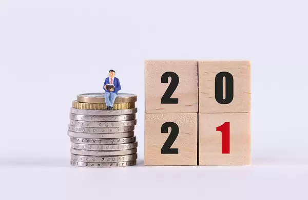 Man sitting on stack of coins and wooden cubes with 2021 text