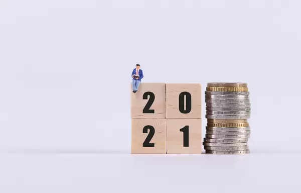 Man sitting on wooden cubes with 2021 text and stack of coins on white background