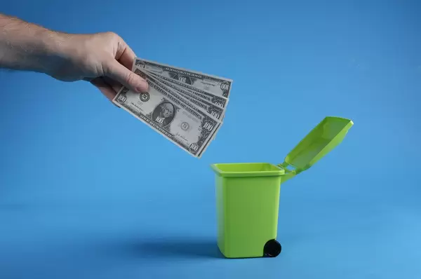 Man throwing away dollars in trashcan