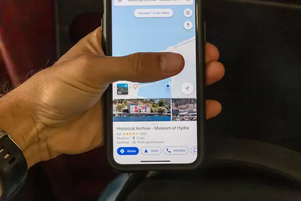 Man uses google maps on his smartphone to check the opening hours of the sight "Historical Archive Museum of Hydra" on the greek island