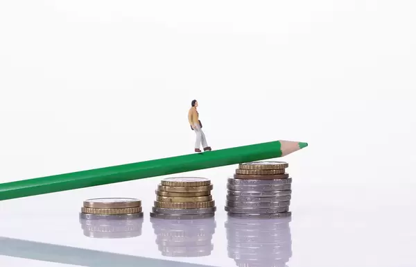 Man walking on a green pencil laying on a stack of coins