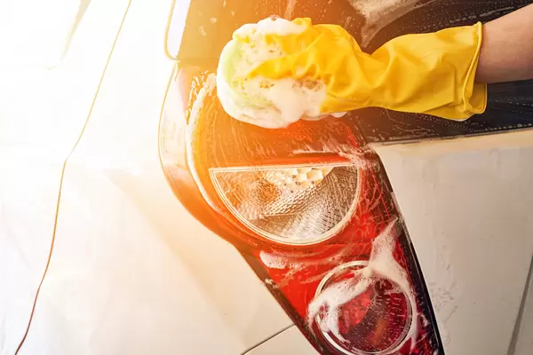 Man washing car rear lights with sponge and foam