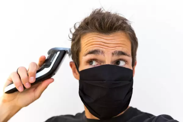 Man with a face mask cuts his own hair with a hair clipper as hairdressers are closed due to the Covid-19 pandemic