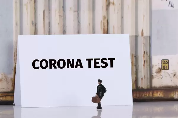 Man with a suitcase standing in front of Corona test text