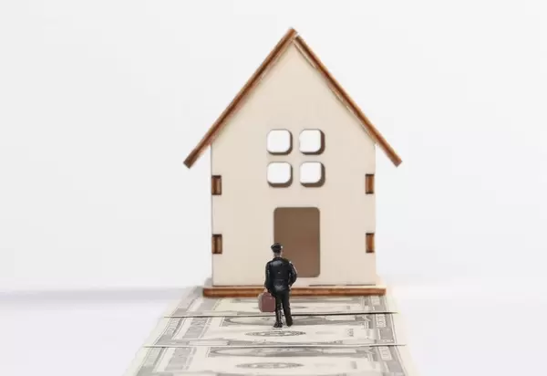 Man with a suitcase standing in front of tiny house on white background