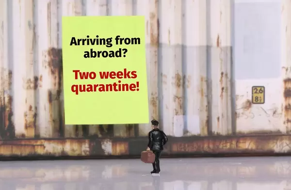 Man with a suitcase standing in front of yellow board with Two weeks quarantine warning