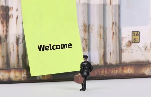 Man with a suitcase standing in front of yellow board with Welcome text