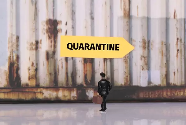 Man with a suitcase standing in front of yellow sign for Quarantine