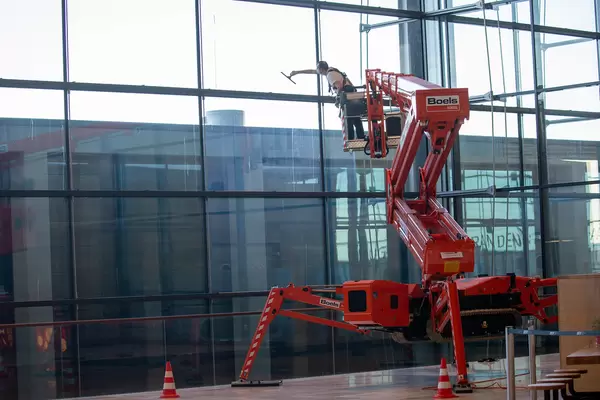 Man with face mask on a red platforms cleans the windows of the newly inaugurated BER airport