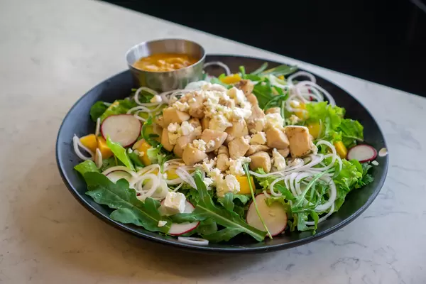 Mango-Curry-Hähnchen Salat mit Rucola, Feta Käse, Avocado, Radieschen und Zwiebeln auf einem Teller in einem Restaurant