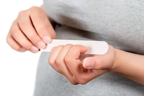 Manicure at home. Women's hands sawing nails at home close up with a manicure nail file