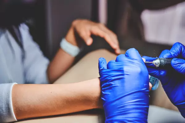 Manicure master removing nail polish with electric machine during manicure procedure