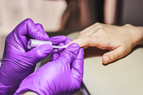 Manicurist applying transparent base coat to nail