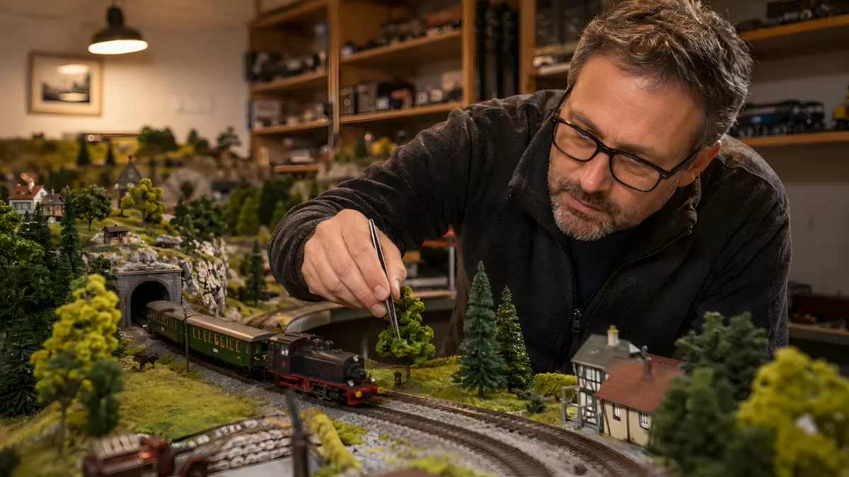 Mann arbeitet detailliert an einer Modelleisenbahn-Anlage