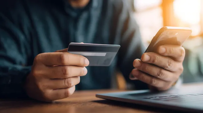 Mann bezahlt mit Kreditkarte und Smartphone am Tisch