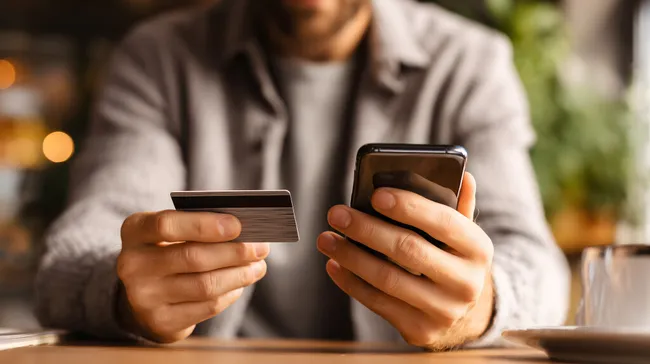 Mann bezahlt Online-Einkauf mit Smartphone und Kreditkarte