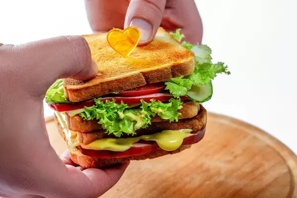 Mann, der Sandwiche mit Schinkenkäsegemüse und Käsesoße hält