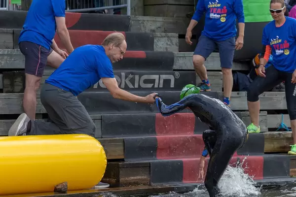 Mann des Ironman-Teams hilft einer Schwimmerin nach der ersten Triathlonetappe aus dem Wasser