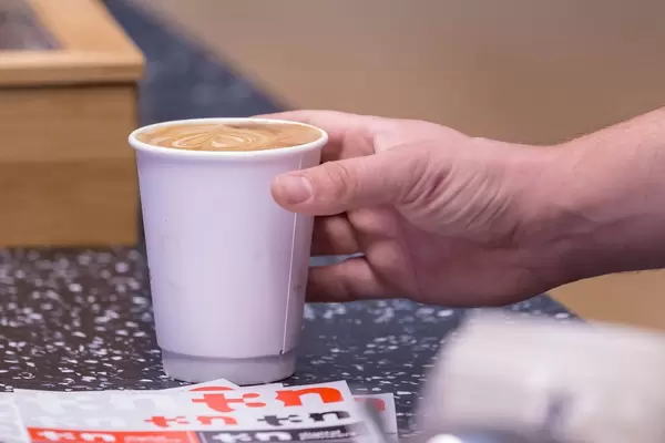 Mann greift nach Cappuccino in Pappbecher