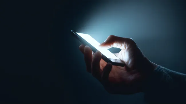 Mann hält leuchtendes Smartphone in dunkler Umgebung