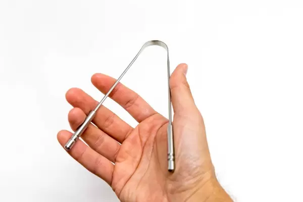Mann hält den Zungenkratzer / Zungenschaber yon Yoga Medic aus Edelstahl für eine gesunde Mundhygiene in der Hand, vor weißem Hintergrund