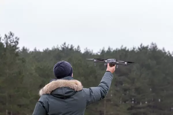 Mann hält Drohne zum Start in die Luft vor Waldstück