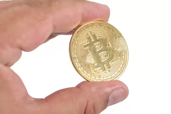 Mann hält eine goldene Bitcoinmünze in der Hand, vor weißem Hintergrund