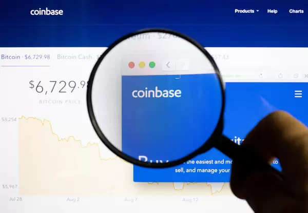 Mann hält eine Lupe über dem Coinbase-Logo