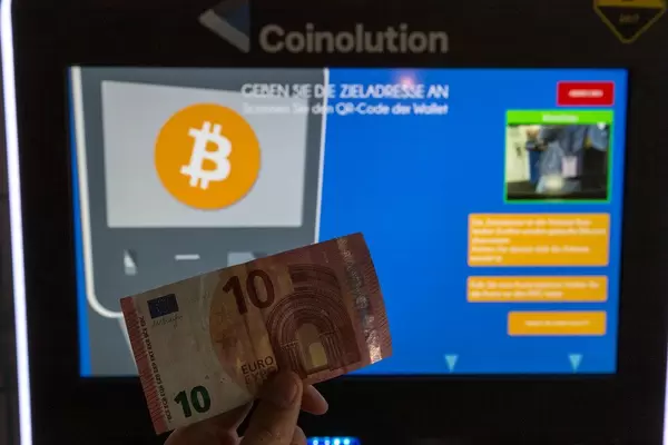 Mann hält einen 10 Euro Schein vor einen Coinolution Bitcoin Geldautomat, um ihn gegen die Kryptowährung einzutauschen