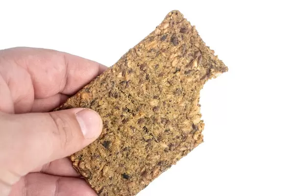 Mann hält einen dunklen Proteinriegel mit Kürbiskernen vor weißem Hintergrund