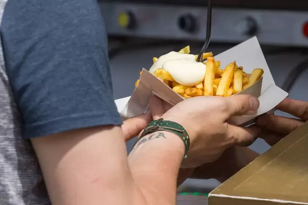 Mann hält Pommes frites mit Mayonnaise auf einem Papierteller auf dem Tomorrowland Festival