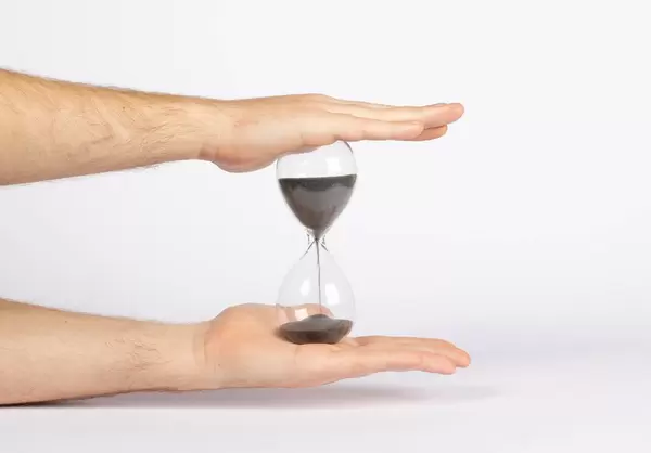 Mann hält Sanduhr mit dunklem Sand zwischen den Händen vor weißem Hintergrund