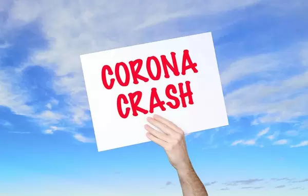 Mann hält Schild mit "Corona crash" Text und blauem Himmel als Hintergrund
