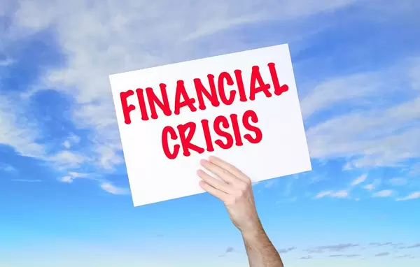 Mann hält Schild mit "Financial crisis / Finanzielle Krise" Text und blauem Himmel als Hintergrund