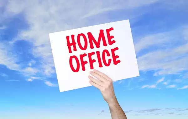 Mann hält Schild mit "Home Office" Text und blauem Himmel als Hintergrund
