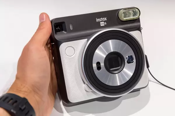 Mann hält Sofortbildkamera Instax Square SQ6 in Pearl White an der Photokina in Köln