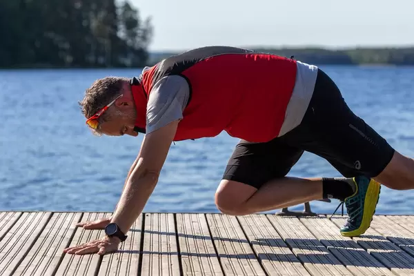 Mann in Asics-Sportlerhoser macht Fitnessübungen auf einer Holzterrasse am Päijänne-See am gleichnamigen Nationalpark in Finnland