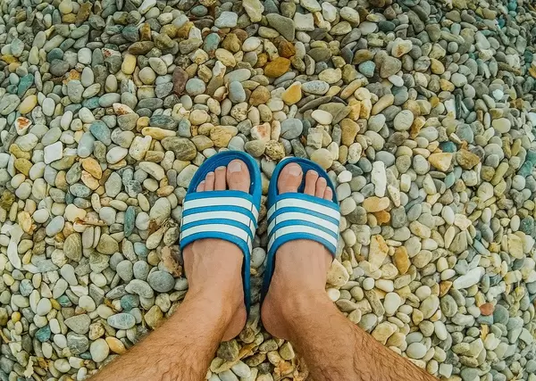 Mann in blau-weißen Badelatschen steht am Strand