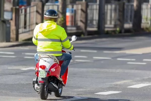 Mann in gelber Jacke fährt Motorroller auf einer leeren Straße