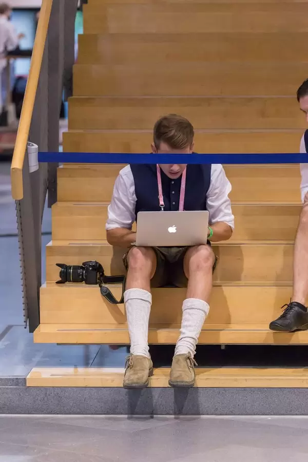Mann in Lederhosen bedient Macbook auf einer Treppe, Absperrung als Zensur