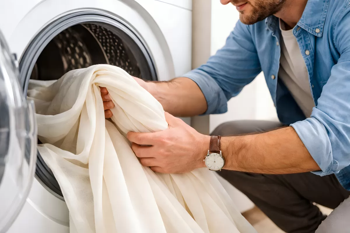 Mann legt weiße Bettwäsche in die Waschmaschine