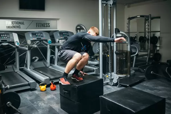 Mann macht Boxsprung in Fitnessstudio mit Laufbändern und Fitnessgeräten im Hintergrund