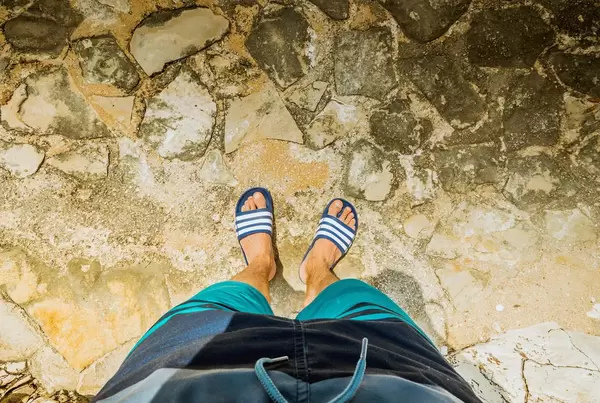Mann mit Badelatschen steht am Strand