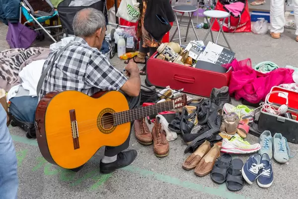 Mann mit Gitarre schaut sich gebrauchte Schuhe am Naschmarkt Flohmarkt an
